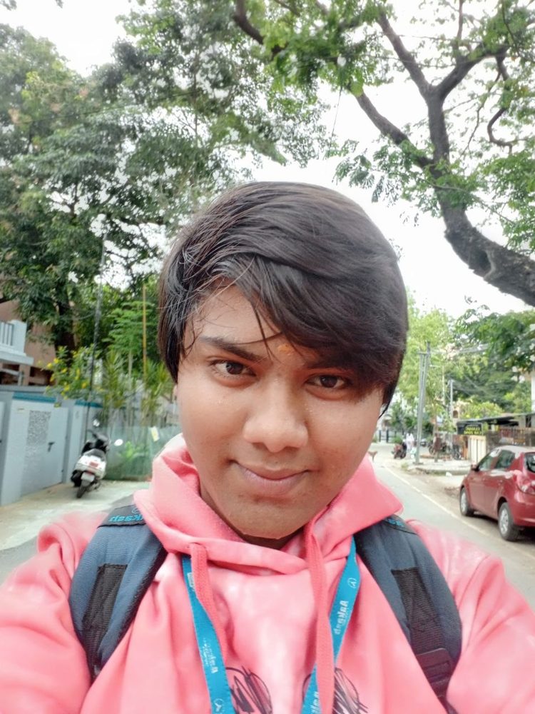 Selfie on a leafy street in a pink hoodie with a backpack